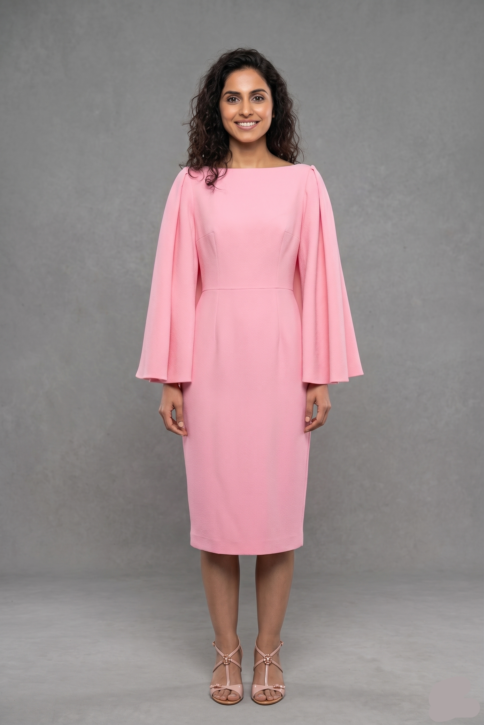 Woman wearing a pink dress with long sleeves against a gray background