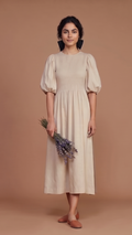 Woman wearing a beige dress holding lavender flowers against a brown background
