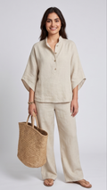 Woman wearing a beige linen outfit holding a straw bag on a plain background