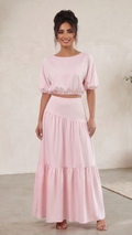 Woman wearing a pink outfit standing in a minimalistic room with a plant.
