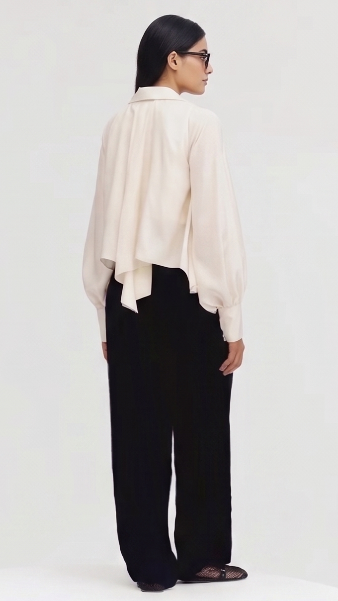 Person wearing a beige blouse and black pants on a white background