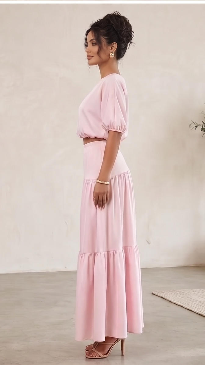 Woman wearing a pink dress standing in a minimalistic room with a plant and abstract sculpture.